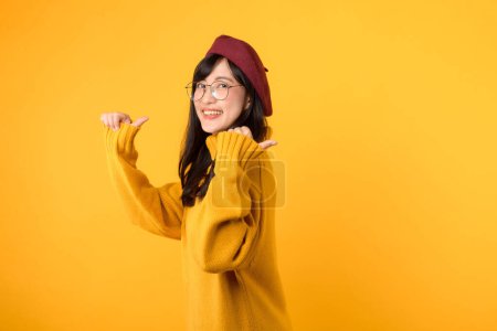 Foto de Joven mujer asiática de 30 años, con camisa amarilla y boina roja. cara feliz y el dedo que apunta a espacio libre copia contra el fondo amarillo vibrante. Desbloquear ahorros y comprar ahora! - Imagen libre de derechos