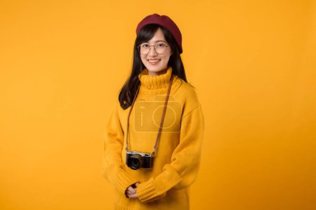 Foto de Con su cámara, la joven asiática, vestida con un suéter amarillo y una boina roja, crea hermosos recuerdos en su elegante estudio. - Imagen libre de derechos