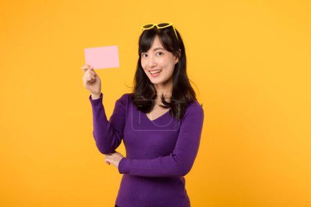 Photo for Wearing purple shirt and sunglasses against a vibrant yellow backdrop, lady displays a blank card board, ready for your message or advertisement. - Royalty Free Image