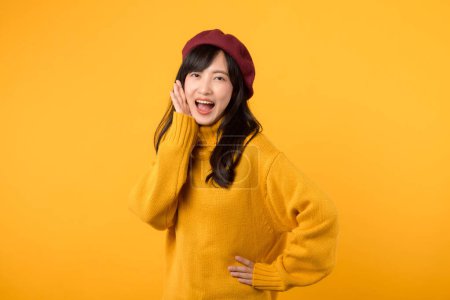Photo for Young Asian woman 30s making a stylish announcement, wearing a yellow sweater and red beret against a vibrant yellow background. Expressive and dynamic communication. - Royalty Free Image