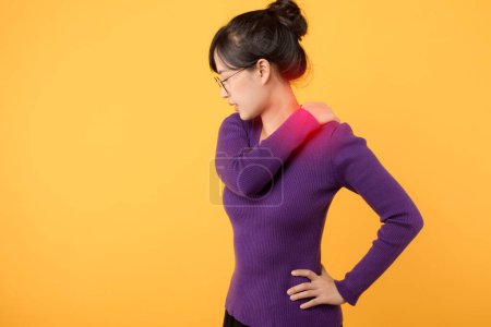 Téléchargez les photos : Portrait d'une femme asiatique, vêtue d'une chemise violette et de lunettes, souffrant de douleurs et de stress musculaires, cherchant une thérapie et un traitement, isolée sur fond jaune. - en image libre de droit