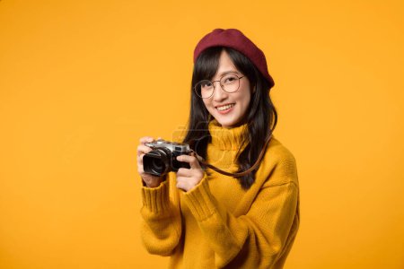 Foto de En su búsqueda por capturar la belleza de la vida, la joven asiática, vistiendo un suéter amarillo y una boina roja, hábilmente empuña su cámara como fotógrafa talentosa. - Imagen libre de derechos