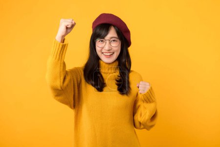 Foto de ¡Expresando victoria con un gesto de puño arriba! Una adolescente de moda, con boina roja y suéter amarillo, celebra contra un fondo amarillo vibrante. - Imagen libre de derechos