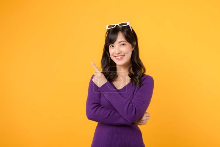 Foto de Hermosa mujer asiática joven con camisa púrpura apuntando hacia arriba para copiar el espacio con la cara sonrisa y feliz. Chica bonita actuar como un producto satisfecho, el uso de la publicidad con fondo amarillo - Imagen libre de derechos