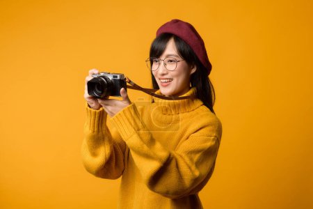 Una joven asiática, fotógrafa apasionada, viaja por el mundo con su cámara, capturando recuerdos. Lleva un suéter amarillo y una boina roja sobre un vibrante fondo amarillo..