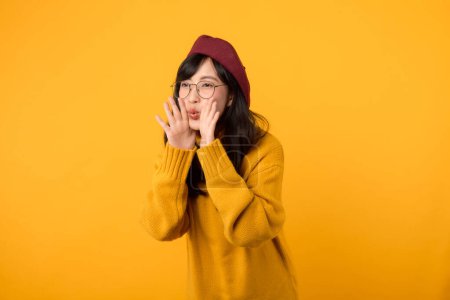 Foto de Get ready for the news! trendy woman, in a red beret and yellow sweater, screams an announcement against a yellow backdrop. - Imagen libre de derechos