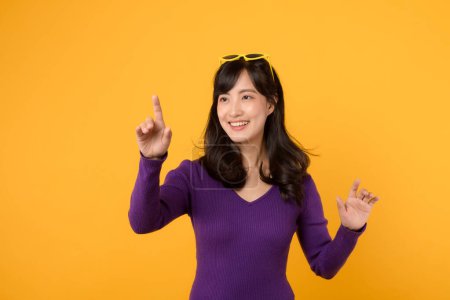 Photo for Young asian woman wearing purple shirt and yellow sunglasses on head happy smile expression touching virtual screen isolated on yellow background. Technology concept. - Royalty Free Image
