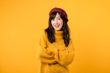 Téléchargez les photos : Positif jeune femme asiatique trentaine, avec les bras croisés sur la poitrine, exsudant confiance dans un pull jaune et béret rouge sur un fond jaune. - en image libre de droit