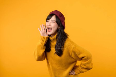 Téléchargez les photos : Communication dynamique. Asiatique femme trentaine annonce avec flair, revêtant un pull jaune et béret rouge sur un fond jaune vif. - en image libre de droit