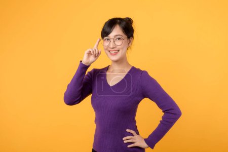 Téléchargez les photos : Femme d'affaires joyeuse portant chemise violette, sur fond jaune réfléchissant avec confiance, explore des idées créatives pour le succès. Expression positive dans l'esprit d'entreprise et l'innovation. - en image libre de droit