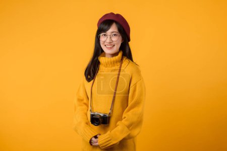 Una joven asiática que captura creativamente recuerdos en suéter amarillo y boina roja sobre un vibrante fondo amarillo.