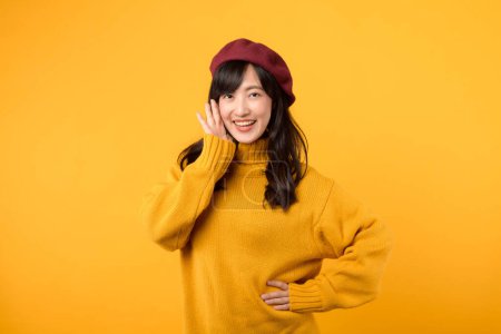Photo for Young Asian woman 30s making a stylish announcement with enthusiasm. wears a yellow sweater and red beret, set against a vibrant yellow background. - Royalty Free Image