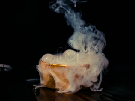 Eis in einer goldenen Schachtel mit Rauch, buntem Rauch, blauem Rauch, grauem Rauch, Eis in Sirup, köstlichem Eis. Raumbild auf dunklem Hintergrund