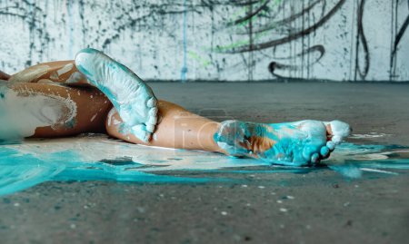 Foto de Hermosas piernas y pies de una sexy joven mujer pintada artísticamente abstracta tumbada en el piso del estudio, bailarina con pintura naranja, azul y turquesa. Arte corporal creativo pintura, espacio de copia. - Imagen libre de derechos