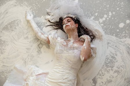 Photo for Upper body of a beautiful sexy young artistically abstract painted woman, bride, in wedding dress, covered with white paint, creative, abstract body art, on the floor in the studio, copy space. - Royalty Free Image