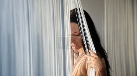 Photo for Portrait of sensual seductive loving dreaming introverted sexy erotic nude woman standing by the window with thread curtain, casts body striped shadows, copy space - Royalty Free Image