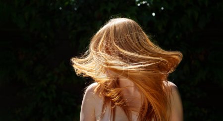 Photo for Wide panorama banner of unrecognizable beautiful sexy redhead woman ginger portrait, shaking her flying long red hair against the dark ivy background in sunny backlight, copy space - Royalty Free Image