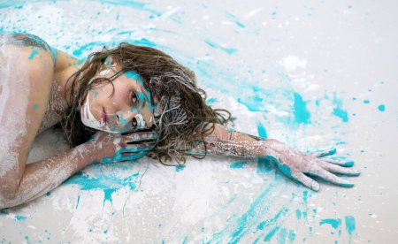 Portrait of sexy nude female woman with long brunette hair, doused with white and turquoise paint, reclining lying, head on arm, elegant on the Studio floor, Copy space