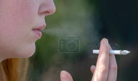 Porträt, Hand, Mund und Hand gezeichnet und von Hand gerollt Zigarette einer jungen süchtigen Frau rauchen fröhlich pustet den Rauch einer Zigarette im Freien, Kopierraum