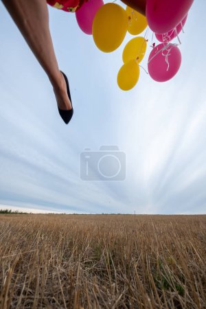 shot from ground below to foot part of a woman with yellow and red balloons running and jumping outdoors in the fields, copy space
