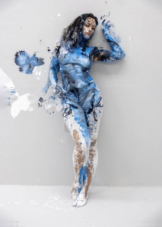 young sexy woman in underwear, sportswear, artistically abstract painted with white, black and blue paint, stands at the studio wall, copy space