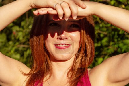 Photo for Young redhead sexy woman shading her eyes with hands and arms in the sunny summer nature in the sun - Royalty Free Image