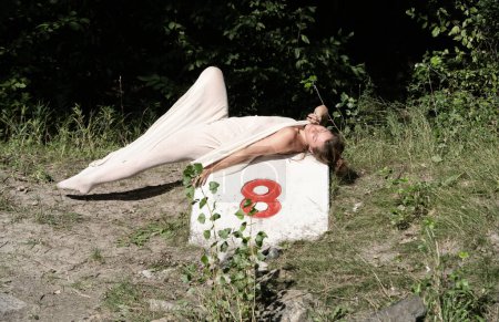 sexy élégante nue fière femme libre, corps enveloppé dans une robe blanche serrée longue peau, repose sur une pierre marqueuse étiquetée avec un 8, à Vienne Danube, espace de copie