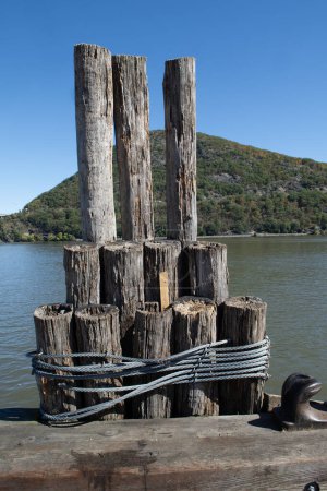 Poteaux d'amarrage anciens attachés avec du fil d'acier sur une jetée de rivière contre une montagne pittoresque