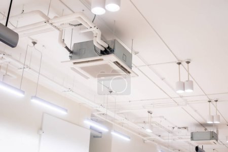 Selective focus to ceiling mounted cassette type air condition units with other parts of ventilation system with hanging lights and other construction parts.