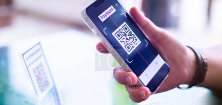 Selektiver Fokus auf die Hand, die das Smartphone hält, um QR-Code auf dem Tag zu scannen. Kunden zahlen per Hand, um digitales Bezahlen ohne Geld zu generieren.
