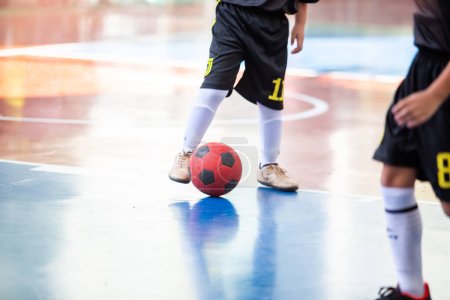 Téléchargez les photos : Kid futsal joueur contrôle la balle pour tirer au but. Salle de sport intérieure de soccer. - en image libre de droit