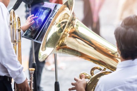 Photo for A musician's hand is touching the screen of a tablet placed on music stand with blurry brass Instruments and wind instrument type. Music band. - Royalty Free Image