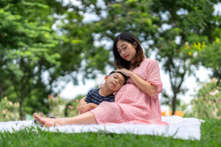Foto de Retrato de una mujer embarazada relajándose en el parque con su hijo. - Imagen libre de derechos