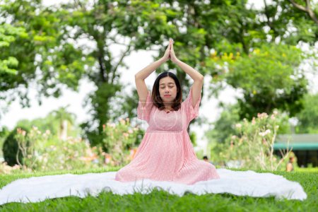 Foto de Retrato de mujer embarazada asiática relajándose haciendo yoga en el parque - Imagen libre de derechos