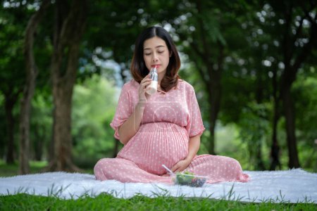 Foto de Retrato de una mujer embarazada asiática bebiendo leche y comiendo ensalada en el parque - Imagen libre de derechos