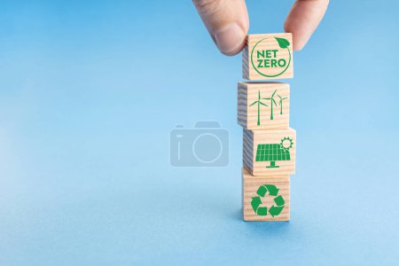 Téléchargez les photos : Net Zero and Carbon Neutral Concept. Hand putting wood block with Net Zero icon on top of others with green energy icons. Blue background. Copy space - en image libre de droit