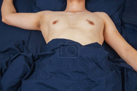 Foto de Handsome young man sleeping comfortably on the bed at night in his bedroom without clothes. Bachelor bedroom. Deep sleep - Imagen libre de derechos