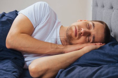 Téléchargez les photos : Top view of a handsome young man sleeping comfortably on the bed at night in his bedroom. Sleep in different positions. Bachelor bedroom. Deep sleep - en image libre de droit