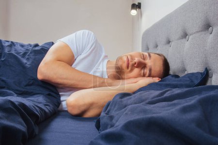Photo for Top view of a handsome young man sleeping comfortably on the bed at night in his bedroom. Sleep in different positions. Bachelor bedroom. Deep sleep - Royalty Free Image
