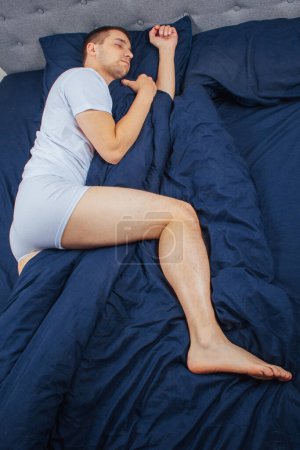 Téléchargez les photos : Top view of a handsome young man sleeping comfortably on the bed at night in his bedroom. Sleep in different positions. Bachelor bedroom. Sleeping on your stomach - en image libre de droit