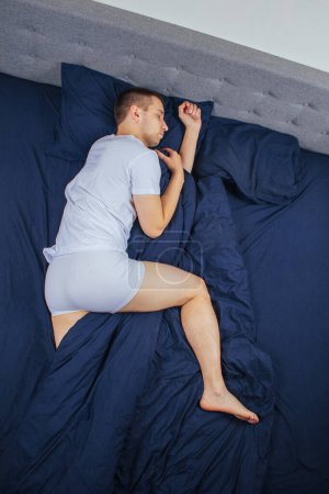 Téléchargez les photos : Top view of a handsome young man sleeping comfortably on the bed at night in his bedroom. Sleep in different positions. Bachelor bedroom. Sleeping on your stomach - en image libre de droit