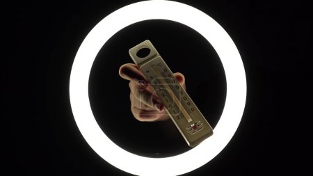 Téléchargez les photos : Plastic alcohol thermometer with a red stripe in female hands close-up on a black background. temperature measurement concept. - en image libre de droit