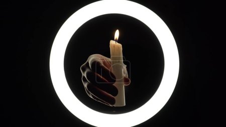 Foto de Female hands light a candle close-up on a black background. burning fire on a candle stick. The concept of ritual actions. - Imagen libre de derechos