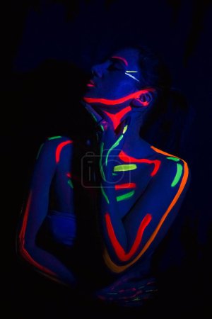 Photo for Fashion model woman in neon light, portrait of a beautiful model with fluorescent makeup, body art design in UV, painted face, colorful makeup, on a black background of a girl. Disco dancer in neon light - Royalty Free Image