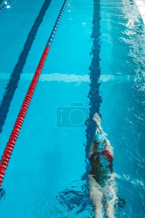 Foto de Vista superior de una joven nadadora entrenando en la piscina, nadando sobre su espalda bajo el agua. Flota bajo el agua y sopla anillos de aire - Imagen libre de derechos