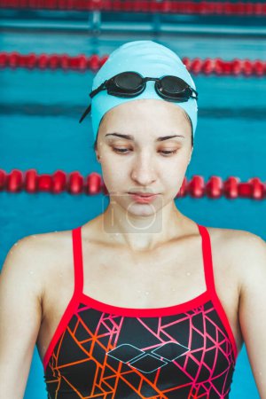 Foto de Mujer nadadora musculosa feliz en gafas y gorra en la piscina y representa el concepto de salud y buena forma. Hermosa modelo femenina en el agua haciendo natación sincronizada - Imagen libre de derechos