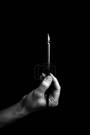 Photo for Female hand elegantly holding an ink pen with a metal tip close-up on a black background. classic fountain pen isolated macro black and white. copy space. vertical. - Royalty Free Image