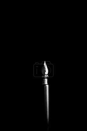 Photo for An ink pen with a metal tip close-up on a black background. classic fountain pen isolated macro black and white. copy space. vertical. - Royalty Free Image