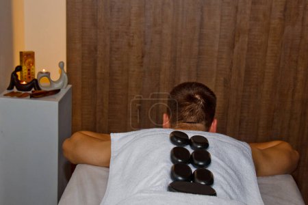 Téléchargez les photos : Concept bien-être. Beau jeune homme relaxant sous l'effet stimulant d'un massage traditionnel aux pierres chaudes dans un spa de luxe et un centre de bien-être. Récupération après le travail - en image libre de droit