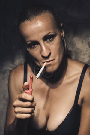 Téléchargez les photos : Femme érotique modèle féminin fumant une cigarette avec ttattoos contre le mur en ville. - en image libre de droit